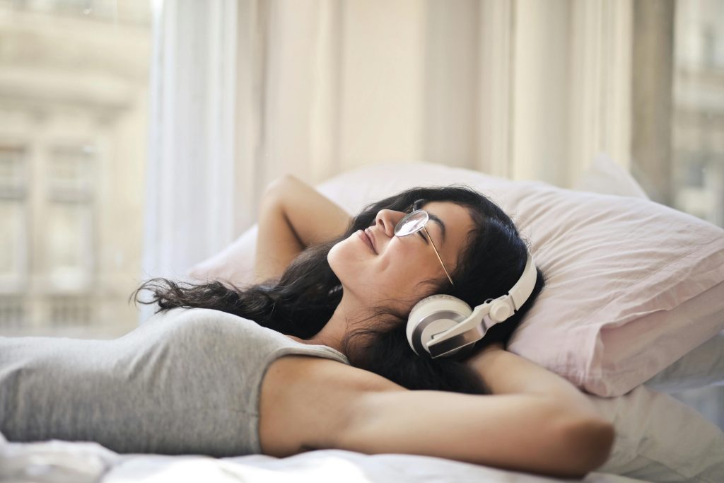smiling woman lying comfortably on a bed, listening to music with headphones